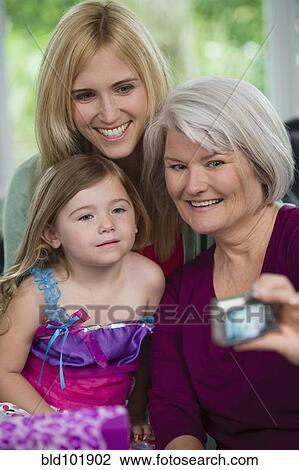 Stock Image - Smiling Caucasian grandmother, mother and daughter taking pictures. Fotosearch