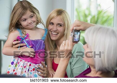 Stock Image - Smiling Caucasian grandmother, mother and daughter taking pictures. Fotosearch