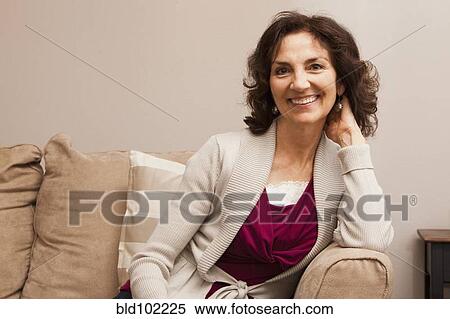 Stock Photography - Smiling Caucasian woman sitting on sofa. Fotosearch