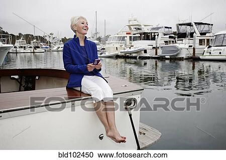 Stock Image - Woman sitting on boat text messaging on cell phone. Fotosearch
