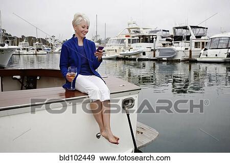 Stock Photo - Woman sitting on boat text messaging on cell phone. Fotosearch