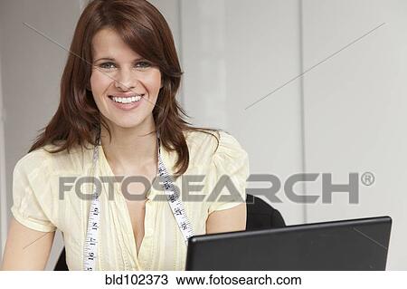 Stock Image - Woman with measuring tape around neck using computer. Fotosearch