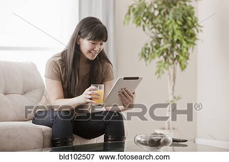 Asian woman drinking orange juice and using digital tablet View Large Photo Image Stock Photo - Asian woman drinking orange juice and using digital tablet. Fotosearch