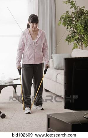 Stock Photo - Asian woman exercising with bands in living room. Fotosearch