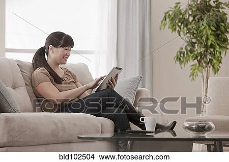 Asian woman sitting on sofa using digital tablet View Large Photo Image Picture - Asian woman sitting on sofa using digital tablet. Fotosearch
