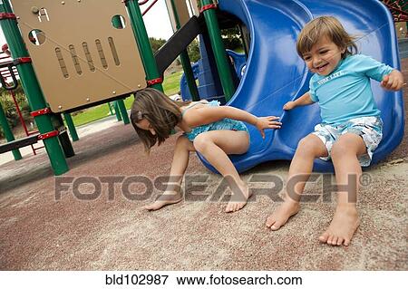 Brother and sister sliding down slide on playground View Large Photo Image Stock Photo - Brother and sister sliding down slide on playground. Fotosearch