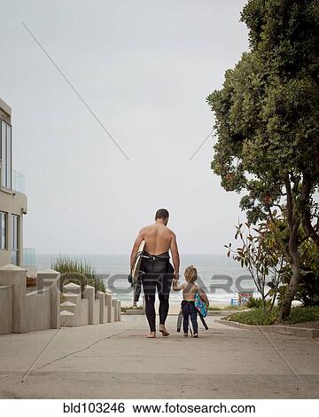 Caucasian father and son in wetsuits walking toward the ocean View Large Photo Image Stock Photograph - Caucasian father and son in wetsuits walking toward the ocean. Fotosearch