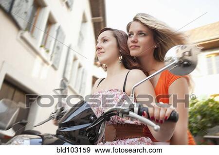Stock Photo - Caucasian friends riding scooter together. Fotosearch