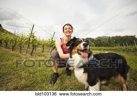 Stock Photograph - Caucasian woman petting dog in vineyard. Fotosearch