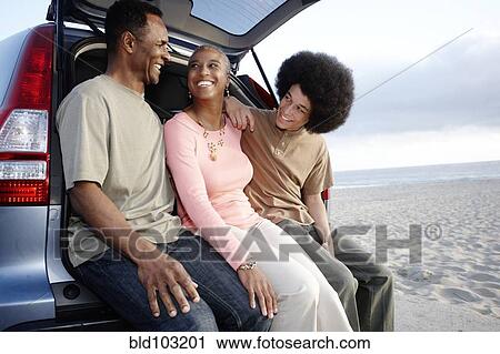 Stock Image - Family sitting on hatchback enjoying the beach. Fotosearch