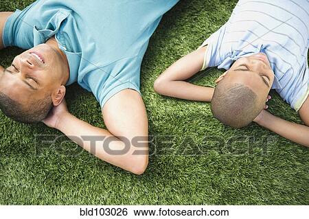 Stock Photograph - Father and son laying in the grass. Fotosearch