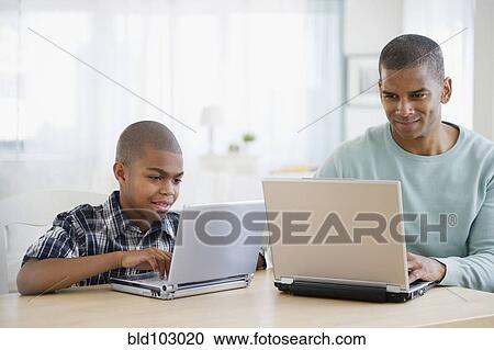 Stock Image - Father and son using laptops together. Fotosearch