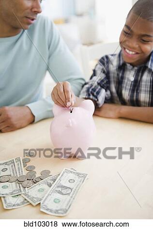 Stock Photo - Father watching son put coin in piggy bank. Fotosearch