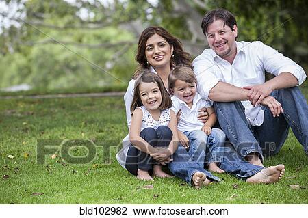 Stock Image - Happy family sitting together in grass. Fotosearch