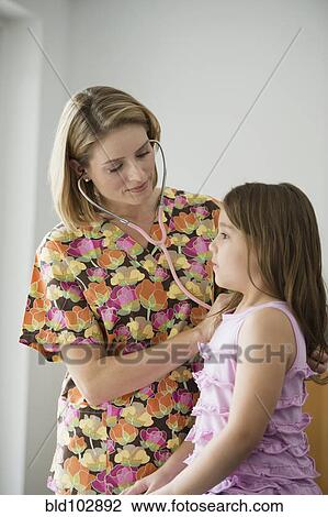 Stock Image - Hispanic nurse listening to girl with stethoscope. Fotosearch