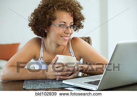 Hispanic woman drinking coffee and using laptop View Large Photo Image Stock Photo - Hispanic woman drinking coffee and using laptop. Fotosearch