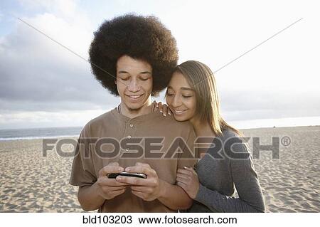 Mixed race couple on beach looking at cell phone View Large Photo Image Stock Image - Mixed race couple on beach looking at cell phone. Fotosearch