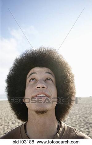 Stock Photo - Mixed race man on beach looking up. Fotosearch