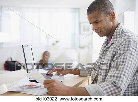 Stock Image - Mixed race man paying bills online. Fotosearch