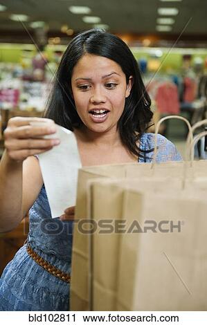 Stock Image - Mixed race woman looking at shopping receipt. Fotosearch