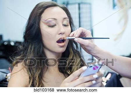 Stock Photo - Mixed race woman with cell phone having make up put on. Fotosearch
