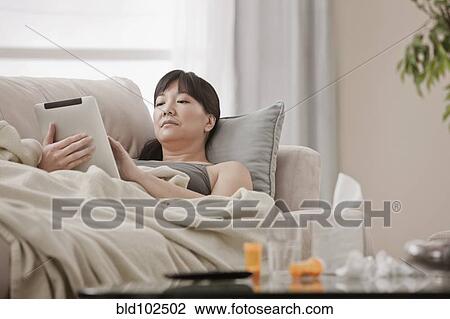 Sick Asian woman using digital tablet on sofa View Large Photo Image Stock Image - Sick Asian woman using digital tablet on sofa. Fotosearch
