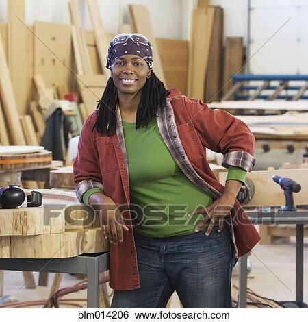 Stock Photograph - Black worker leaning on wood in factory. Fotosearch