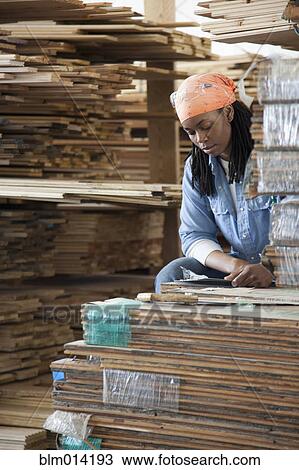 Stock Image - Black worker standing near lumber in warehouse. Fotosearch