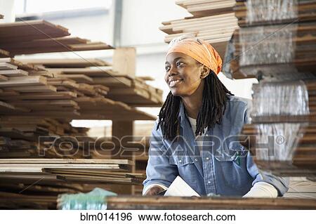 Stock Photograph - Black worker standing near lumber in warehouse. Fotosearch