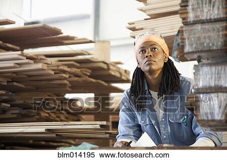 Stock Photography - Black worker standing near lumber in warehouse. Fotosearch