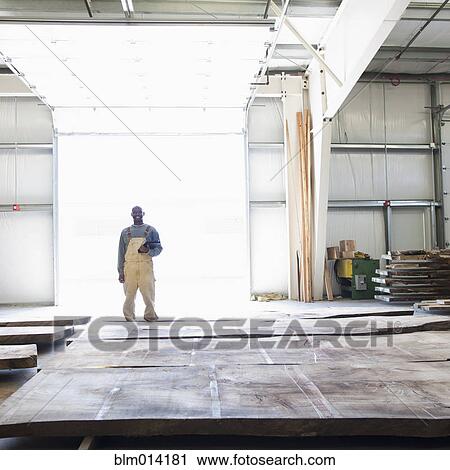 Stock Image - Black worker standing with lumber in warehouse. Fotosearch