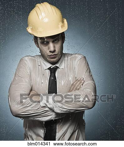 Stock Image - Caucasian businessman in hard-hat standing in rain. Fotosearch