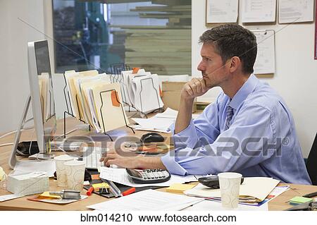 Stock Image - Caucasian businessman working at desk in factory. Fotosearch