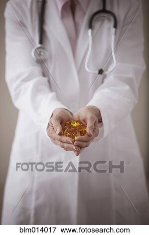 Stock Photo - Caucasian doctor holding pills. Fotosearch