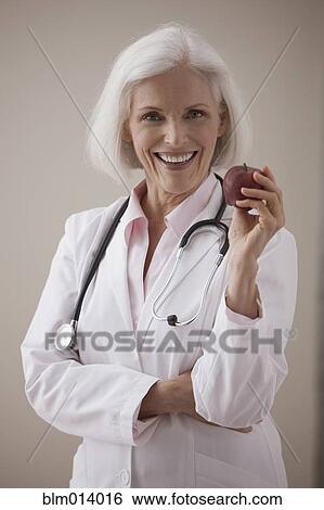 Stock Photograph - Caucasian doctor holding red apple. Fotosearch
