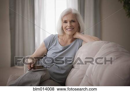 Stock Photo - Caucasian woman sitting on sofa with digital tablet. Fotosearch