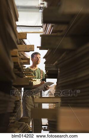 Stock Image - Caucasian worker checking lumber in warehouse. Fotosearch