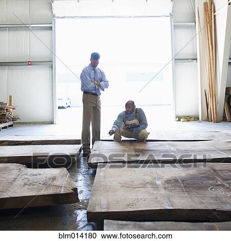Stock Image - Co-workers checking lumber in warehouse. Fotosearch
