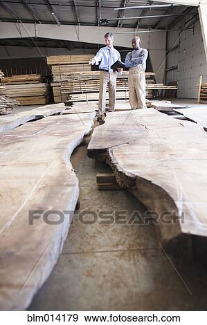 Stock Photo - Co-workers checking lumber in warehouse. Fotosearch