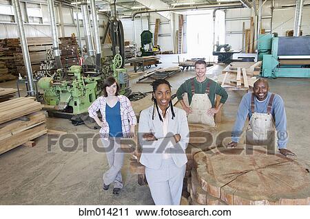 Stock Image - Co-workers standing together in lumber warehouse. Fotosearch