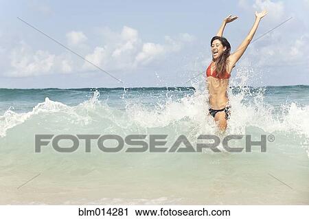 Stock Image - Mixed race woman enjoying ocean waves. Fotosearch