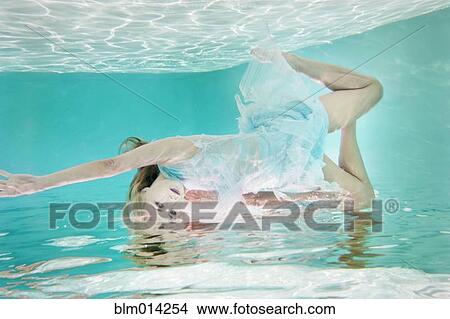 Picture - Mixed race woman in dress underwater in swimming pool. Fotosearch