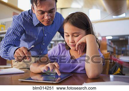Stock Image - Teacher helping student use digital tablet. Fotosearch