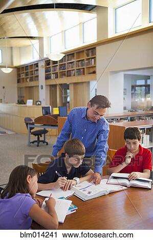 Stock Image - Teacher talking to students in library. Fotosearch