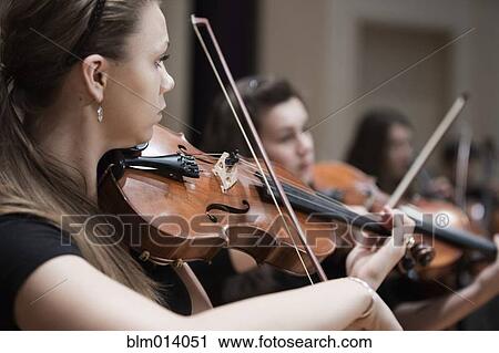 Stock Image - Woman playing violin in orchestra. Fotosearch