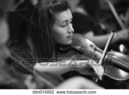 Stock Image - Woman playing violin in orchestra. Fotosearch