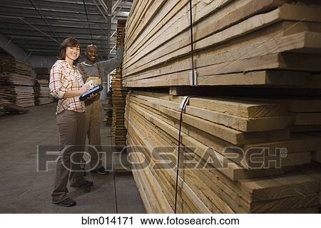 Stock Image - Workers standing near stack of lumber in warehouse. Fotosearch
