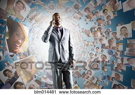 Stock Image - African American businessman on cell phone in front of images of business people. Fotosearch