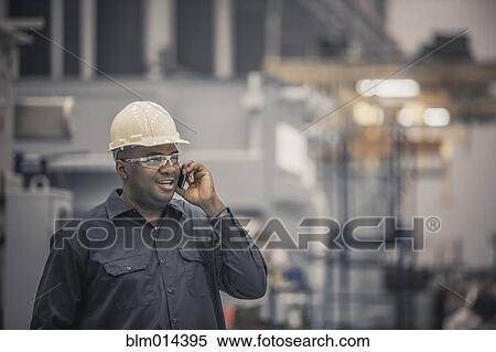 Stock Photography - African American worker using cell phone in factory. Fotosearch