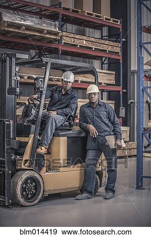 Stock Photo - African American workers with forklift in factory. Fotosearch